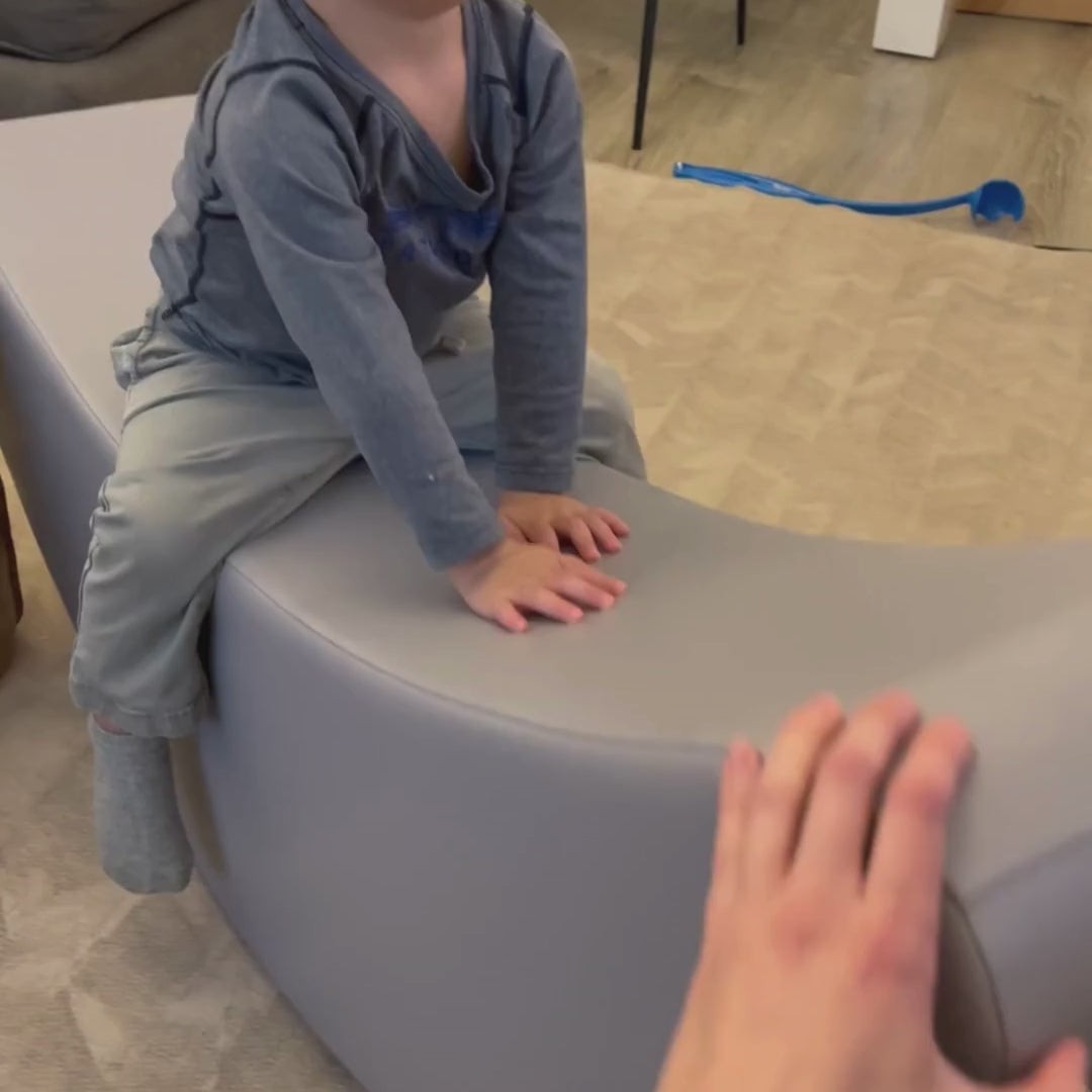 smiling toddler rocking on a playful grey banana toy in a bright playroom