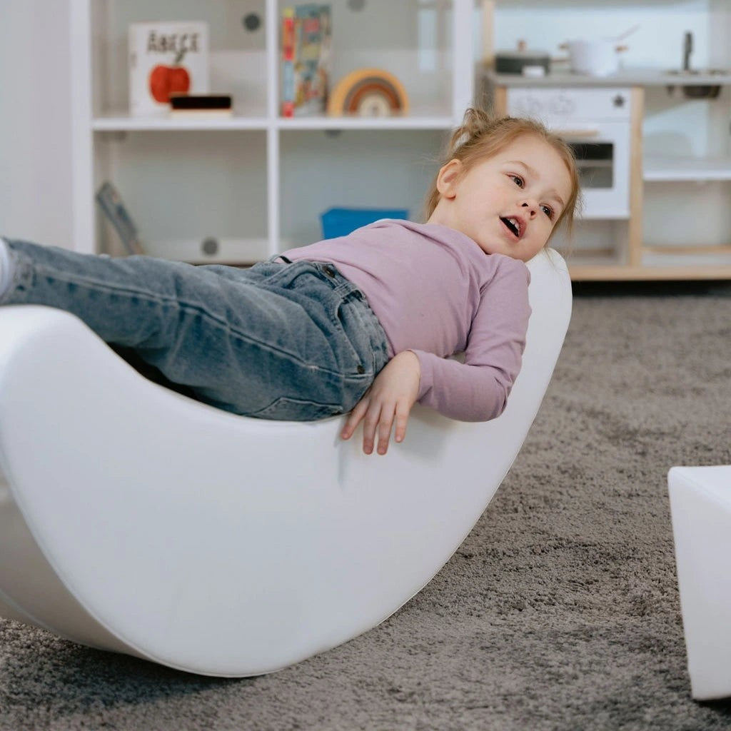 adorable toddler giggling on a soft white banana rocker, boosting balance and joy