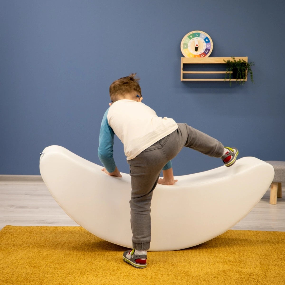 smiling toddler rocking on a soft white banana toy, giggling with joy in a sunlit playroom