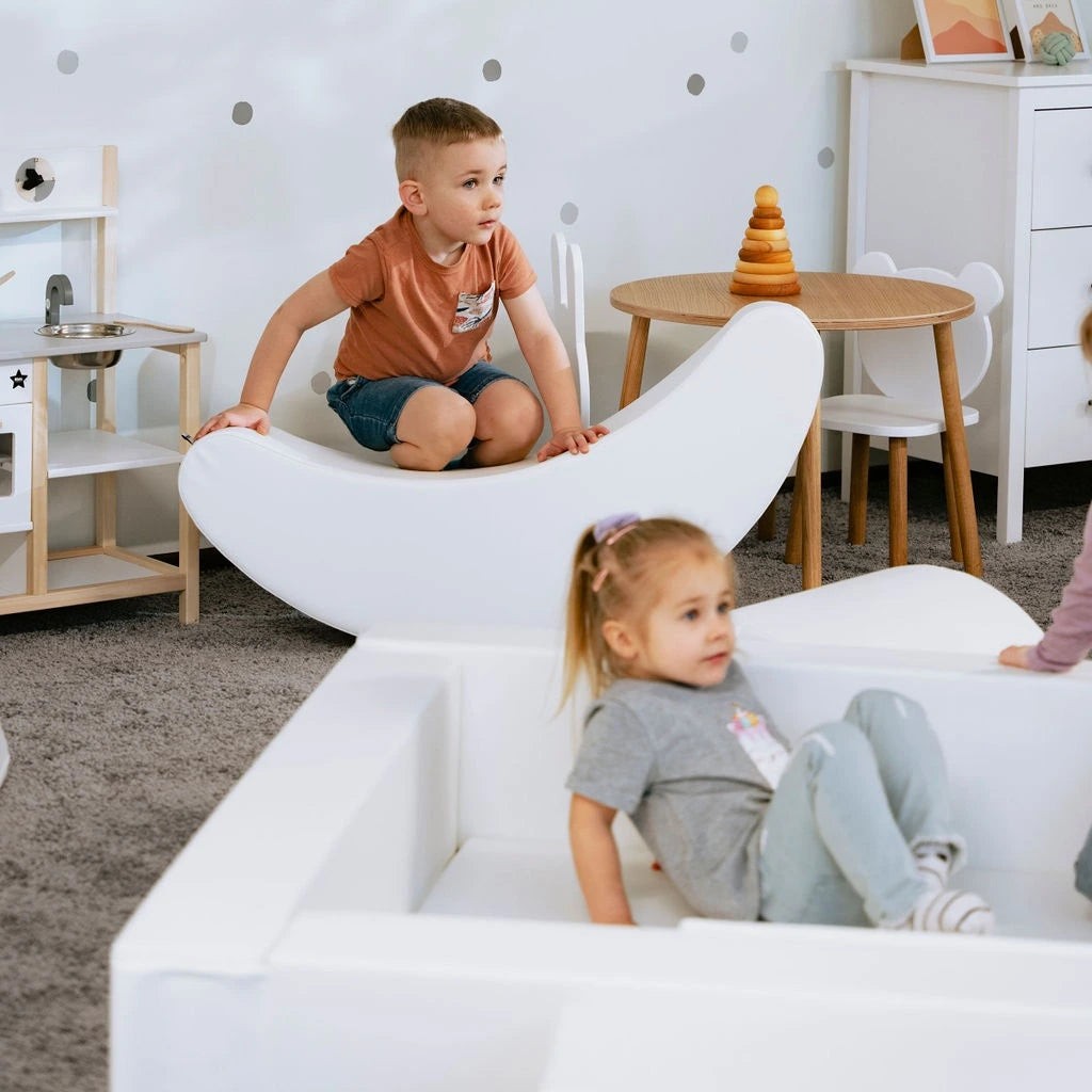 a happy toddler rocking on a soft white banana toy, giggling with delight in a sunlit playroom
