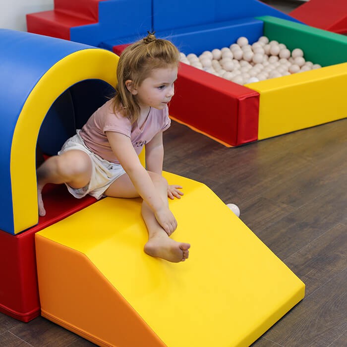 a child peeking through the vibrant multicolor soft play tunnel set during a fun indoor adventure