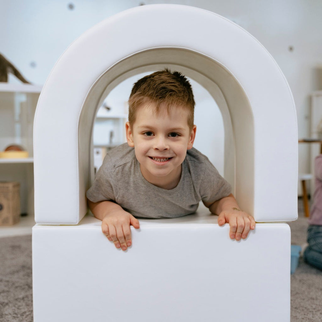 a joyful toddler peeking out from the iglu soft play tunnel with a bright smile