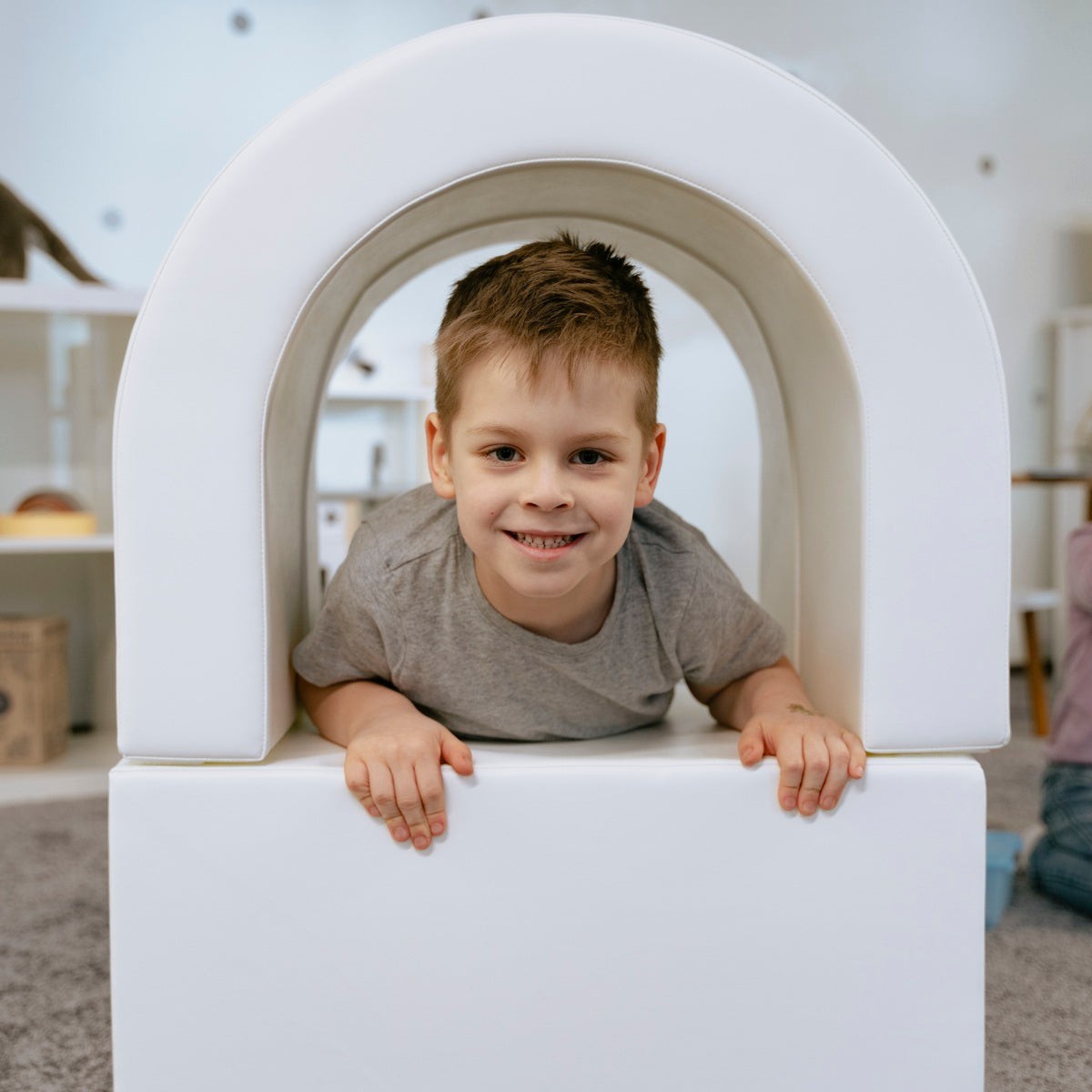 a joyful toddler peeking out from the iglu soft play tunnel with a bright smile