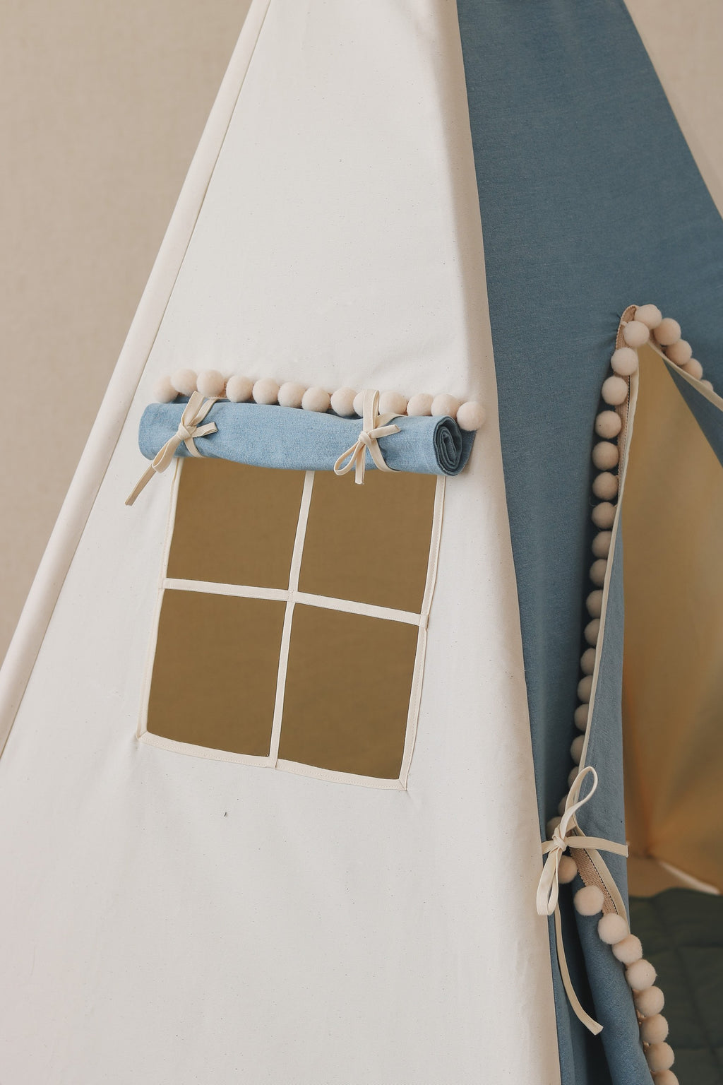 a playful cotton teepee tent with pompoms, open to reveal its cozy interior and curtained window