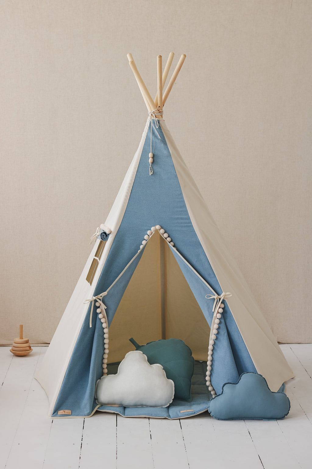 kids denim teepee tent with playful pompoms, folded neatly into its cotton storage cover for easy transport