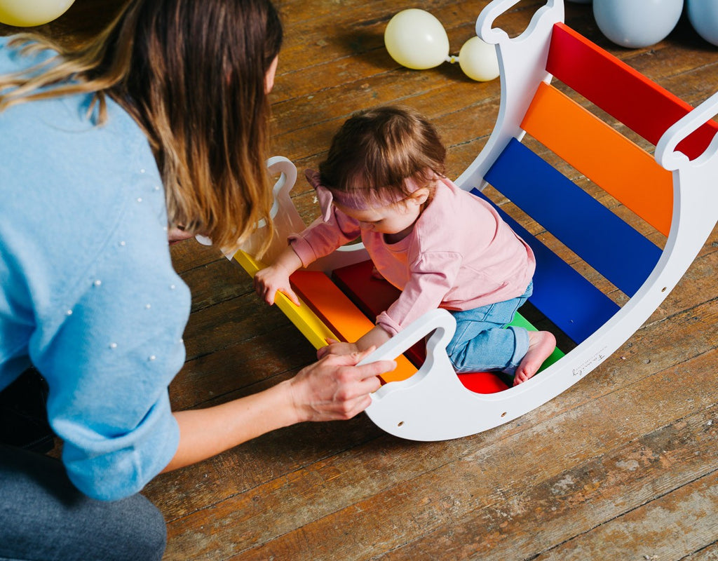 a child's hand gently touching the vibrant birch plywood curve of the rainbow climber swing