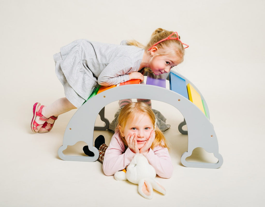 a child's hand reaching for the vibrant rainbow climber swing in a sunlit playroom