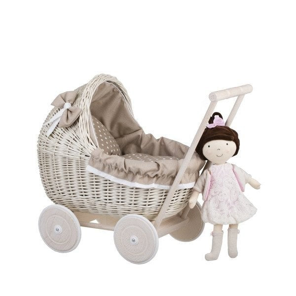 a child's hand gently tucking a doll into the beige bedding of a whitewashed wicker pram