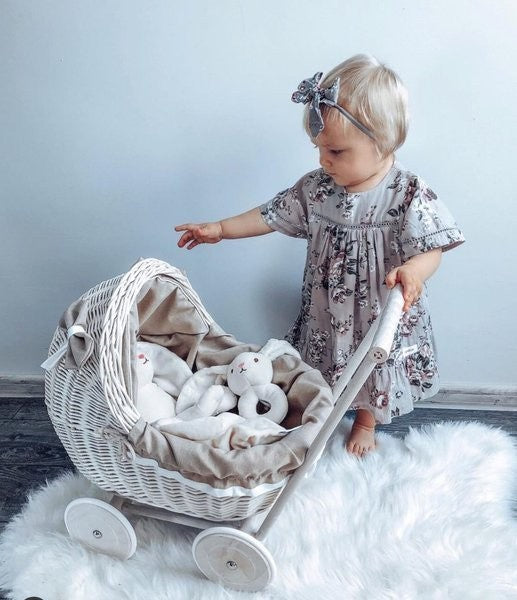 functional whitewashed wicker doll pram with beige bedding, shown from a practical side angle