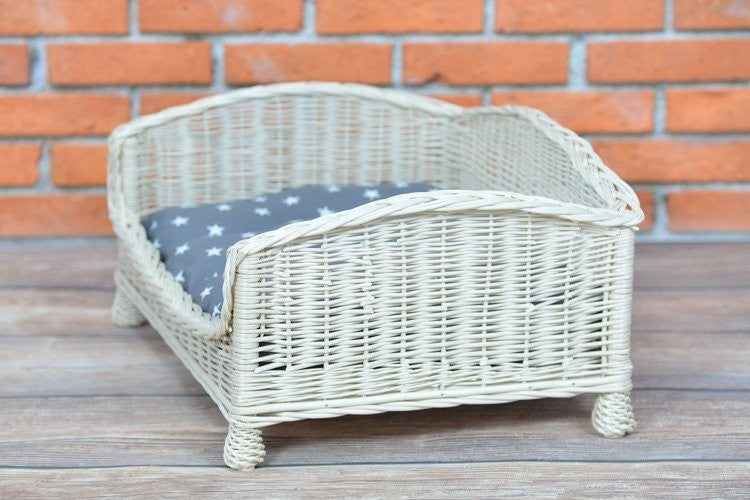a playful puppy peeking over the low front edge of a cozy whitewashed wicker pet bed