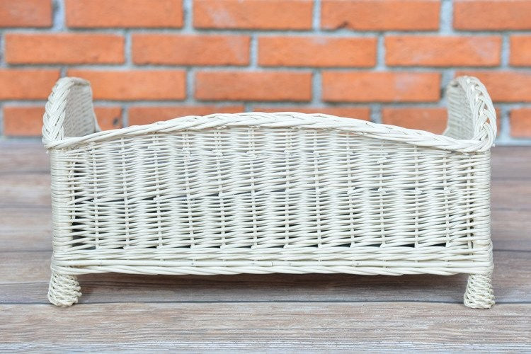 a playful kitten peeking over the low edge of a whitewashed wicker pet bed with a soft cushion