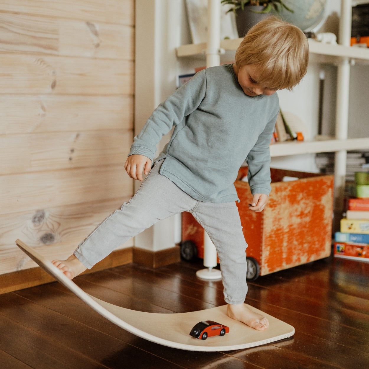 a child gently rocking on a curved wooden balance board in a softly lit, cozy playroom