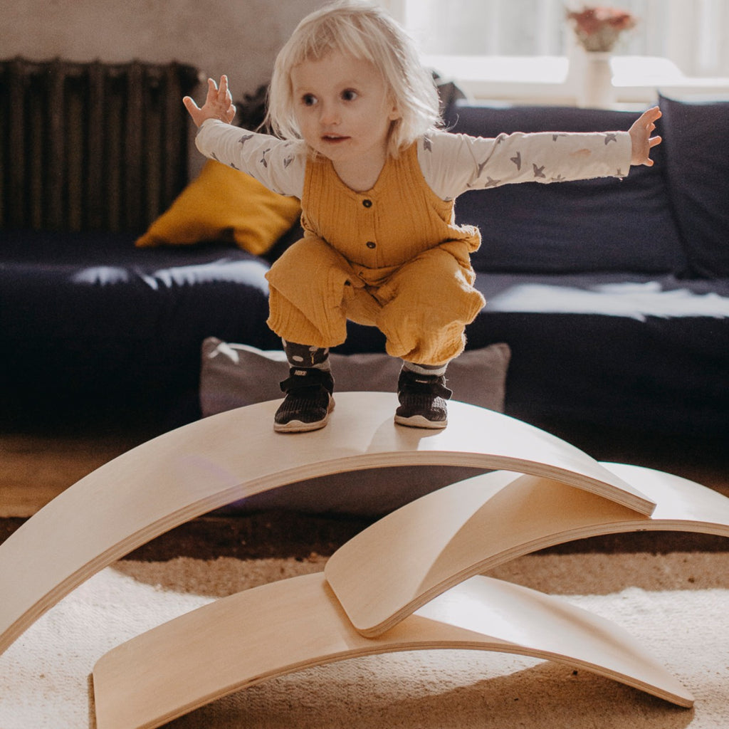 a child laughing while wobbling on a wooden balance board in a sunlit playroom