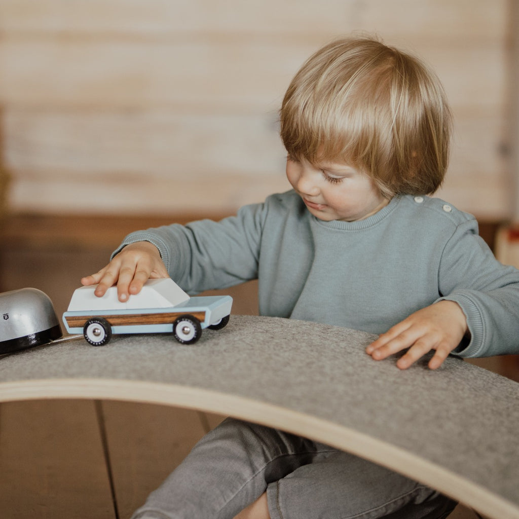 a wooden balance board with grey felt being used as a functional bridge for toys