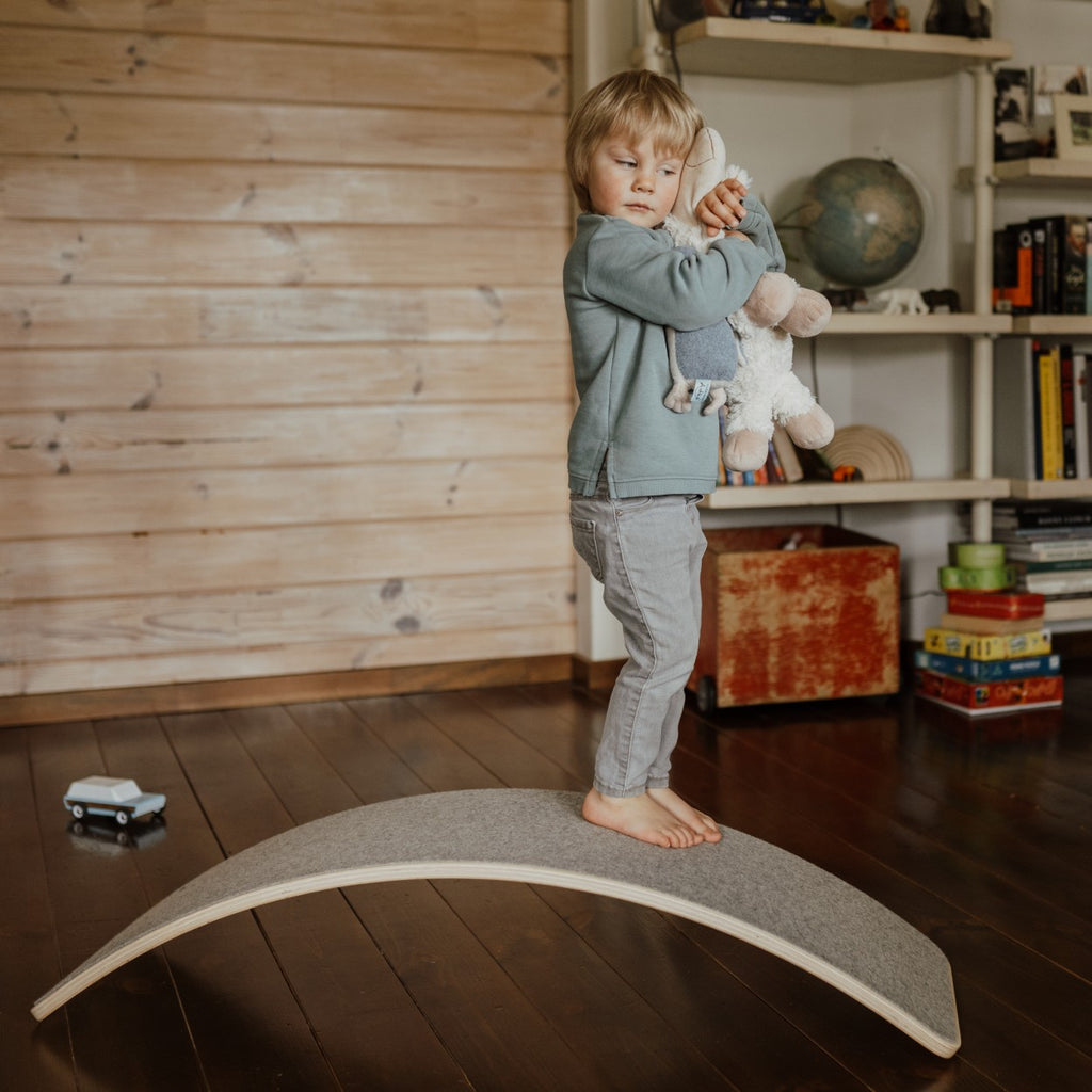a child's feet wobbling on a grey felt balance board in a sunlit playroom