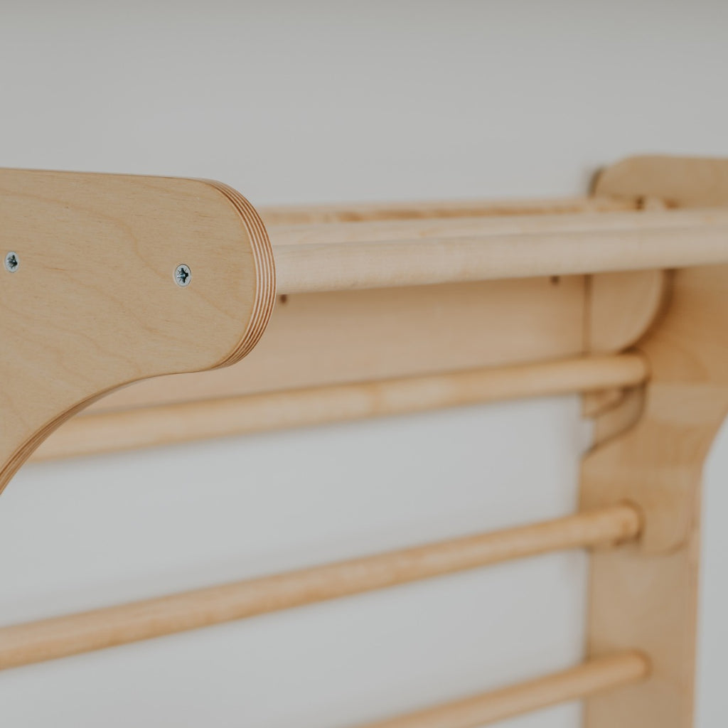 a child's hand reaching for the top rung of the birch pikler triangle in warm morning light