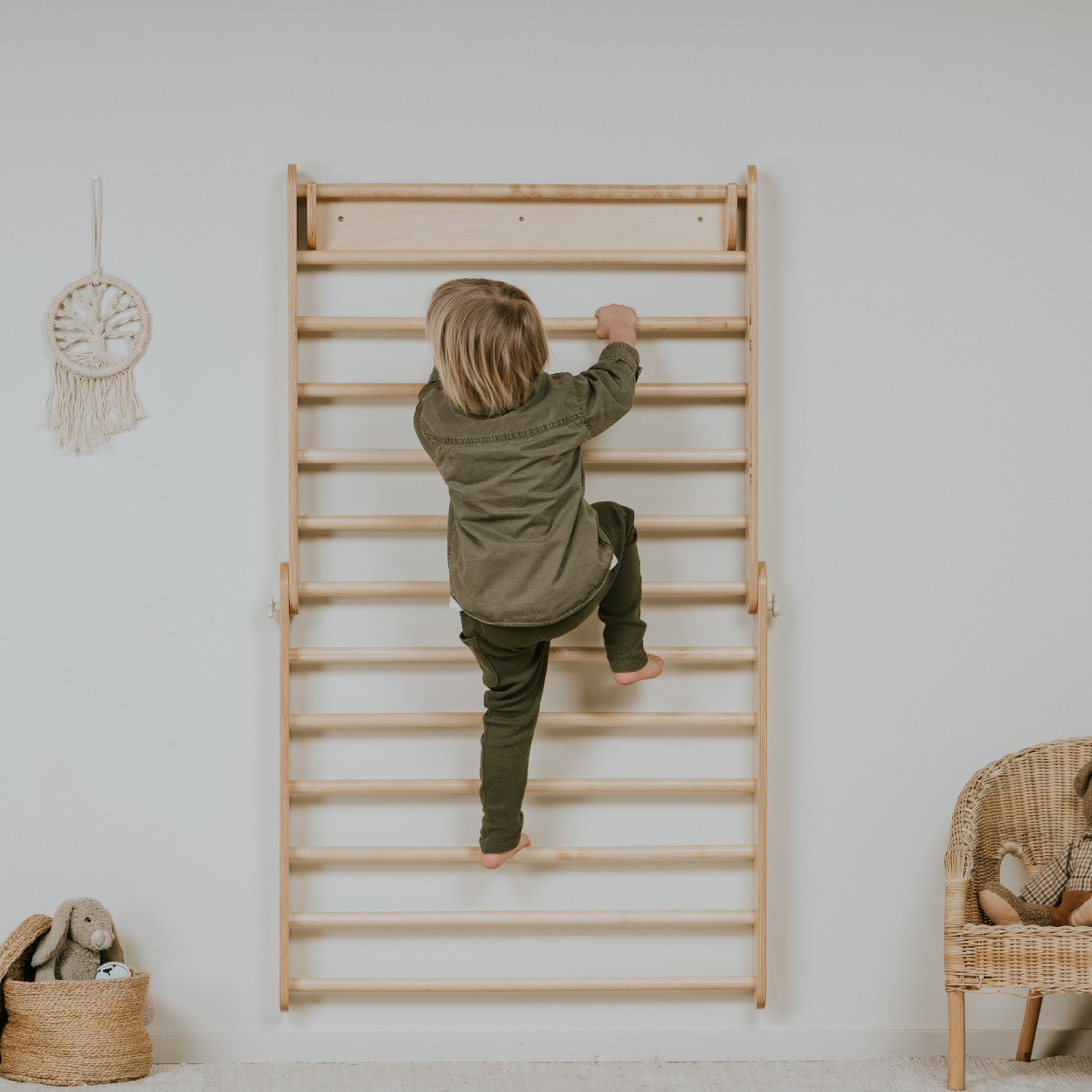 a child's hand gently resting on the warm birch rungs of the pikler triangle in soft morning light