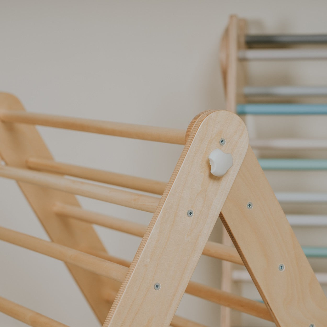 a child's hand reaching for the top rung of the birch pikler triangle in warm morning light