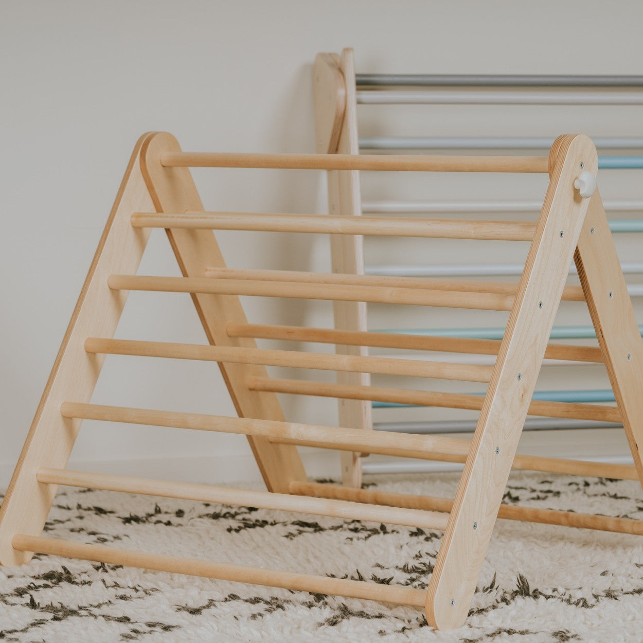 a child's hand gripping the birch rung of a pikler triangle in warm, soft-focus light