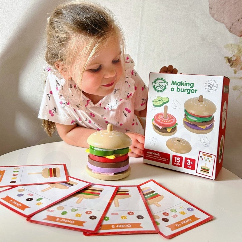 close-up of a child's hands stacking a sustainable wooden burger puzzle with lettuce and tomato