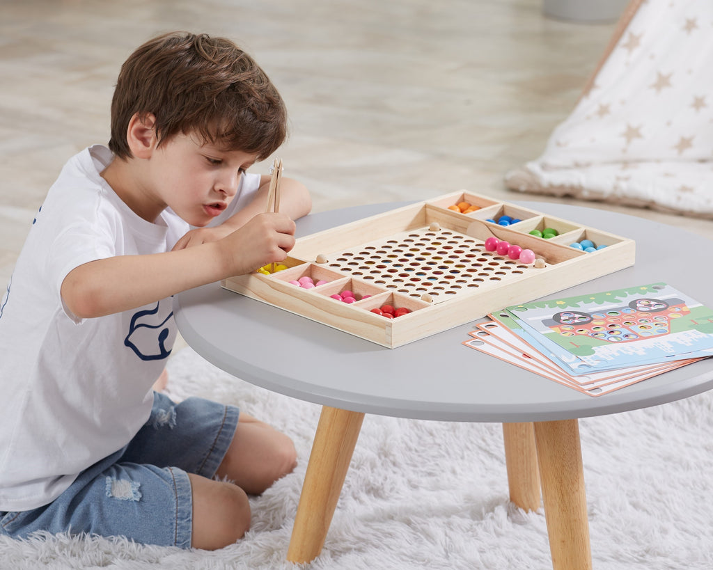 close-up of a child's hands using wooden chopsticks to place colorful beads on a montessori puzzle board