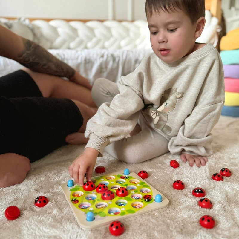 close-up of a child's hands playing with a colorful ladybug memory puzzle on a wooden table
