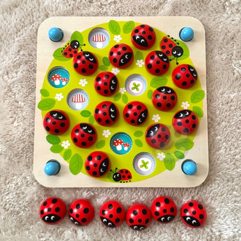 close-up of a child's hand placing a ladybug memory puzzle card on a wooden board