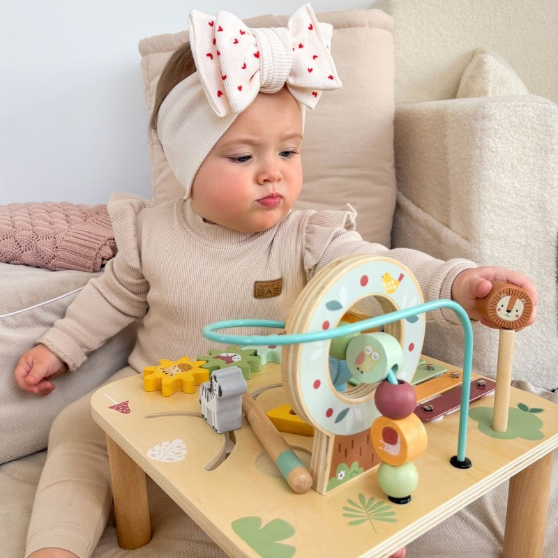 a toddler's hands playing with the colorful ball track and gear spinner on the woopie green activity table