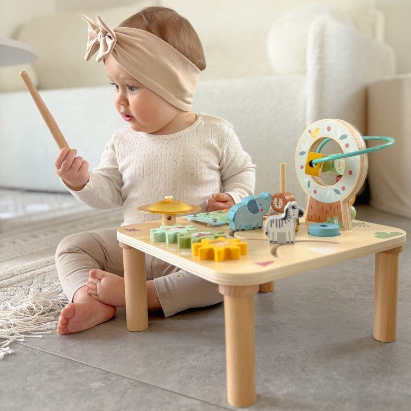 a toddler's hands playing with the colorful ball track on the woopie green wooden activity table