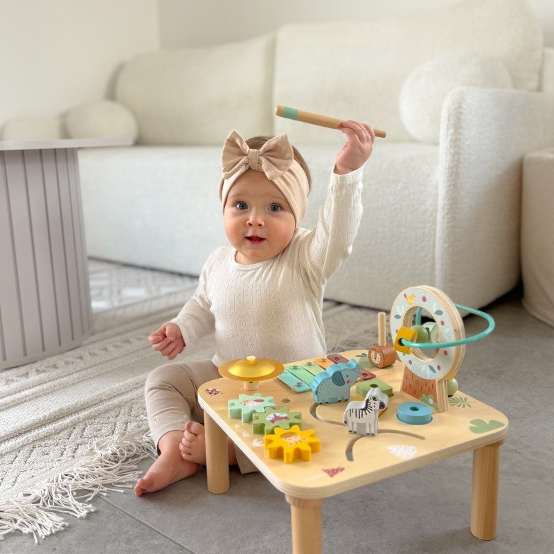 a toddler's hands playing with the colorful ball track on the woopie green wooden activity table