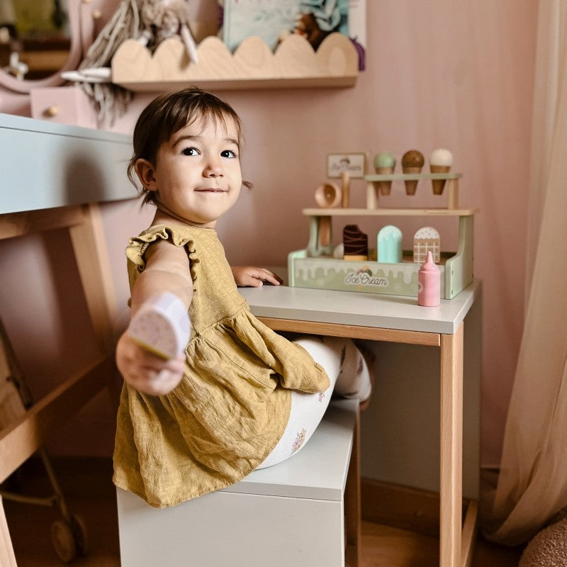 a child's hand playfully stacking colorful magnetic ice cream scoops on a green wooden cone