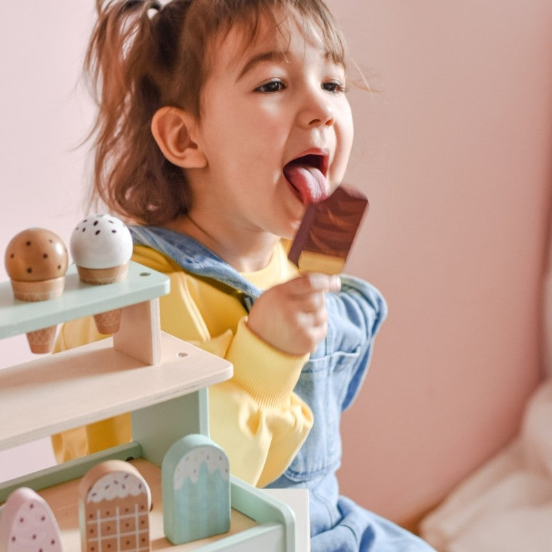 a child's hands carefully stacking magnetic ice cream scoops on a green wooden cone