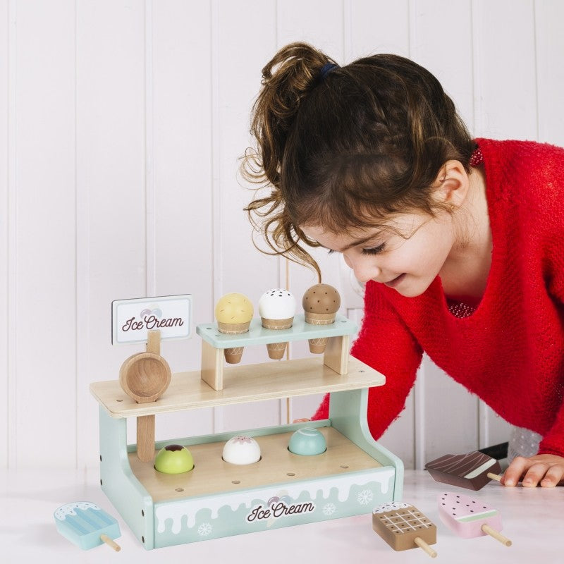 a child's hand carefully placing a magnetic wooden ice cream scoop on a vibrant green stand